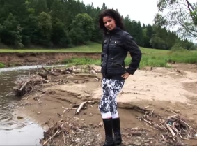 Oksana is playing in the river wearing capri leggings, boots and a black jacket.